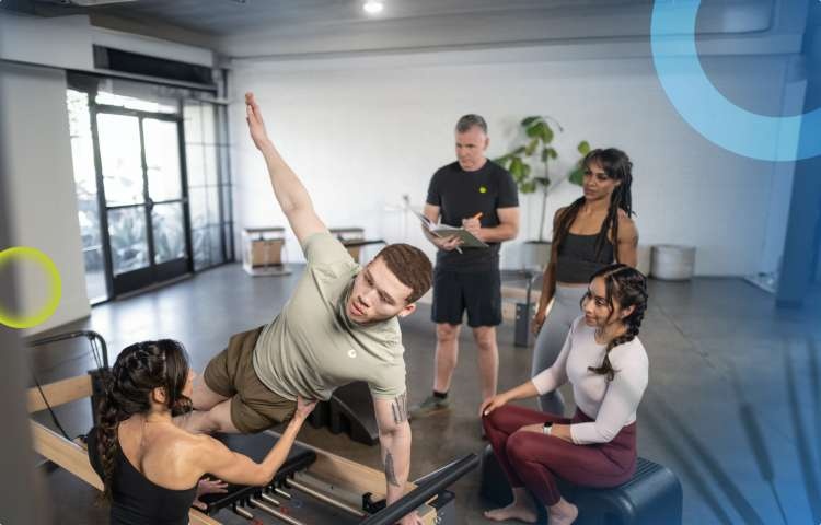 Group of people gathered around Pilates equipment in a studio setting.