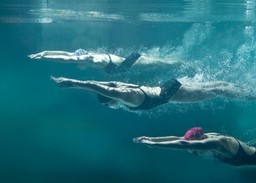 three female swimmers wearing swim caps and googles underwater in a pool